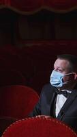 Sad man in medical mask in empty theater. Rich man in suit sitting alone among empty red armchairs and sleeps in opera hall. Lockdown concept. Vertical video