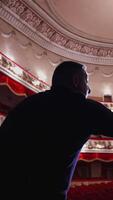 Man talking on a scene of a large theatre. Actor practising on stage before the performance in empty auditorium. Back view. Vertical video
