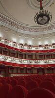 Large theatre hall with nobody. Rows of comfortable armchairs without people in the opera house. Empty red velvet seats inside a theater at pandemic. Vertical video