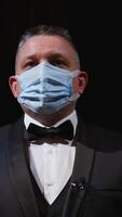Man in elegant suit and medical mask. Portrait of an actor in protective facial mask standing on stage of a theater. Man putting off mask from face. Coronavirus pandemic. Vertical video