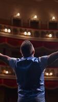 Man performing with gestures on stage. Unrecognizable actor standing on stage in classic theater. Male actor speaks from the scene. Back view. Vertical video