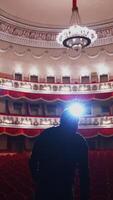 Man on stage in empty theater. Back view of an actor standing on stage and performing in a large theater without people. Vertical video