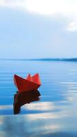 Ship of red paper floating in the blue river at clear day under the blue sky. One paper boat swims on the calm lake in summer Vertical video