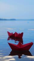 Childish paper boats floating on the water surface on the blurred background. Three red homemade ships on the river Vertical video