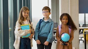 Portrait of three successful diverse pupils with a book and globe in classroom video