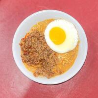 top view spicy curry noodle with beef and sunny side up egg topping on red background photo