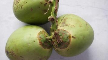 Three green coconuts with leaves on a white surface video