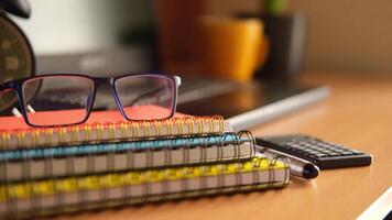 A stack of notebooks, glasses and a calculator on a desk video