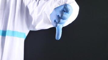 A person in a white coat and blue gloves is holding a thumb up video
