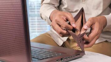 A man is holding a wallet in front of a laptop video