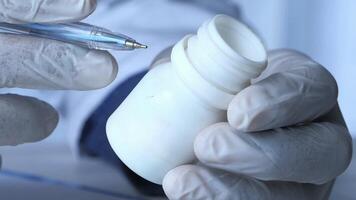 A person in a lab coat holding a pen and a white container video