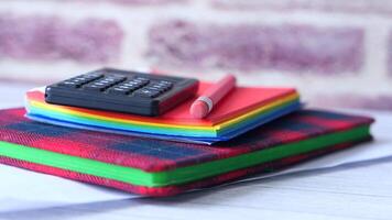 A stack of colorful notebooks and a calculator video