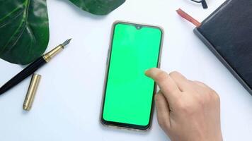 Hand holding a smartphone with a green screen on a white table video