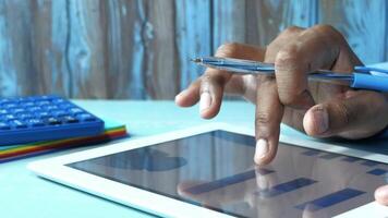 A man's hand is holding a pen and tablet computer in front of a calculator and a pen video