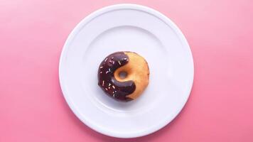 A chocolate donut on a white plate on a pink background video