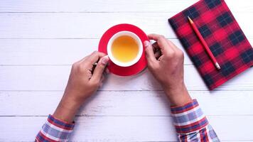 A man's hands holding a cup of tea and a notebook on a white wooden table video