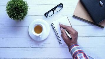 A man writing in a notebook with a cup of coffee and a notebook on a wooden table video