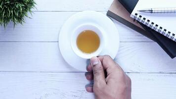 A hand holding a cup of tea on a white table with a notebook and a cup of coffee video