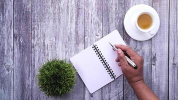 A man's hand writing in a notebook with a cup of tea on a wooden table video