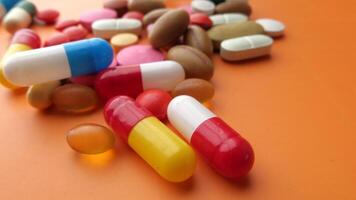 Many different colored pills and capsules on an orange surface video