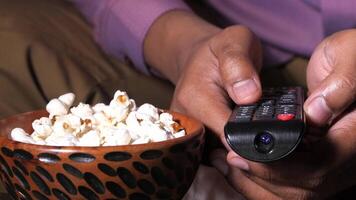 A person holding a remote control over a bowl of popcorn video