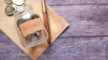 Budget jar with coins and pen on wooden table video
