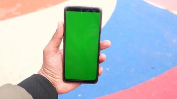 A man in an urban setting holds a smartphone with a green screen, showcasing modern technology video