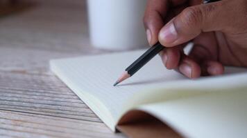 A person writing in a notebook with a pencil on a wooden table video