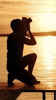 un joven fotógrafo estaba allanamiento y fotografiando el puesta de sol en el puente de el río cerca banco después cuales él izquierda ese lugar. vertical video