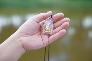 Hand holds Buddha amulet. Concept, faith and belief of Buddhist for holy to protect from dangers, bring good luck, business prosperity and wealth. Collecting amulet as hobbies, exchange, sell or buy. photo
