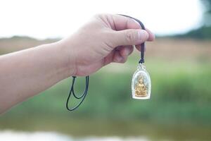 Hand holds Buddha amulet. Concept, faith and belief of Buddhist for holy to protect from dangers, bring good luck, business prosperity and wealth. Collecting amulet as hobbies, exchange, sell or buy. photo