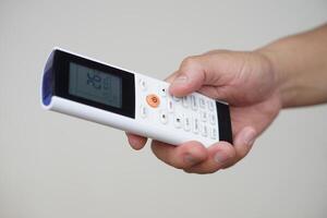 Close up hand hold remote control of air conditioner. Concept, electronics equipment, a remote control can be used to operate devices or appliances with variety functions. Adjust temperature mode. photo