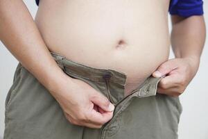 Close up man tries to zip up his trousers for wearing with big belly. Concept, obesity. Health problem, overweight in men cause to diseases. photo