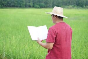 Asian man farmer is reading book at paddy field. Concept, self study, reading book for self development to apply knowledge in daily life living. Agriculture lifestyle. photo