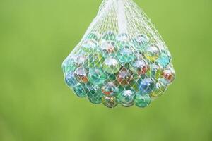 Close up net bag of marbles balls, small spherical object often made from glass. Green background. Concept. object use as toy for playing games or use for DIY craft decoration. photo