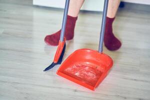 Close up of a plastic dustpan and red broom on the floor with unrecognisable woman, professional cleaner, worker with copy space. Concept of cleaning home, sweeping floor, cleaning dust photo