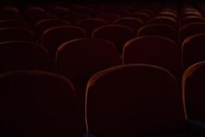 Close up of orange, red seats in dark cinema hall with copy space. Background with rows of chairs with selective focus. Concept of theatre, event, show, presentation, conference, audience photo