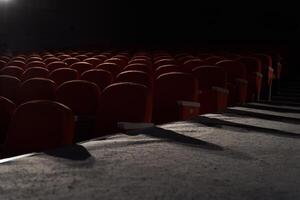 Side view of orange, red seats in dark cinema hall with copy space. Background with rows of chairs with light beam with. Concept of theatre, event, show, presentation, conference, audience photo