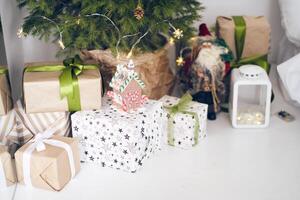 Side view of gifts wrapped in recycled and printed paper, craft, with bows, gingerbread house with candy, Santa under christmas tree, background, copy space. Concept of merry christmas, holiday photo