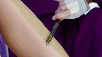 Applying warm wax. Resolute salon worker having depilation procedure and covering legs with special wax material. Vertical video