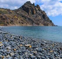 Kara-Dag, volcanic rocks near the Black Sea coast in the national park, rounded pebbles on the beach, Crimea photo