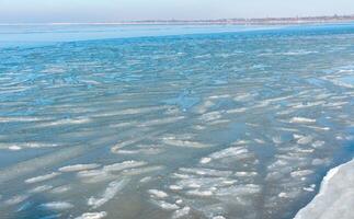 Ice floating near the shore in the form of oblong ice floes, rolled around by waves and a storm in the Tiligul estuary photo