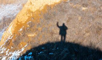 Black shadow, silhouette of a man with a raised hand on the shore of the estuary in winter photo