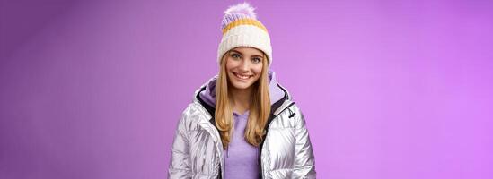 Cute young blond european woman wearing warm cozy jacket hat ski resort vacation having fun smiling amused rent equipment wanna learn snowboarding standing happily purple background photo