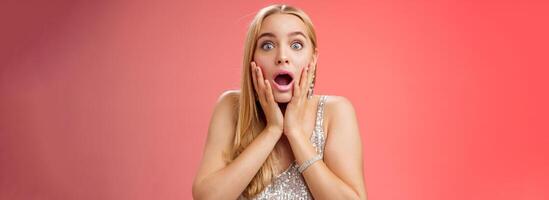 Shocked speechless concerned young stunned woman gasping screaming worried drop jaw touch cheeks widen eyes surprised nervously staring camera troubled afraid, standing red background photo