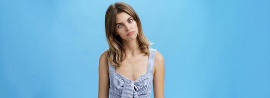 Funny girl squinting eyes to look at nose standing cute and silly over blue background in matching outfit fooling around from boredom trying spent free time aping, posing over blue background photo