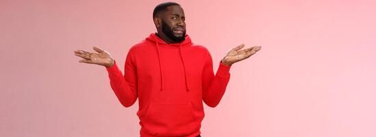 African american man cringe shake head unaware frowning grimacing aversion dislike shrugging hands raised sideways have no idea, standing dissatisfied unpleasant question, clueless pink background photo