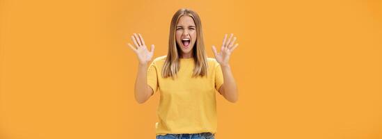 Woman releasing stress yelling with joy and pleasure gesturing with raised arms being daring and rebellious not afraid to show emotions standing passionate and expressive against orange background photo