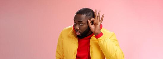Curious funny charismatic black bearded guy bending forward hold hands ear eavesdropping wanna overhear girlfriend conversation behind door standing curious gossiping pink background photo