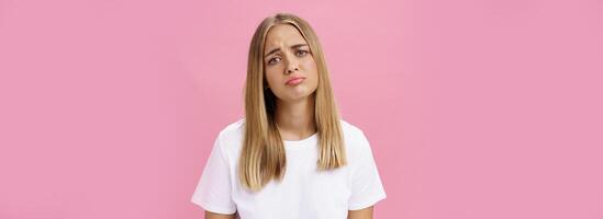 Sad girl whining tilting head raising eyebrows in upset expression and pursing lips feeling disappointed and envy, regretting missed chance standing unhappy and moody over pink background photo